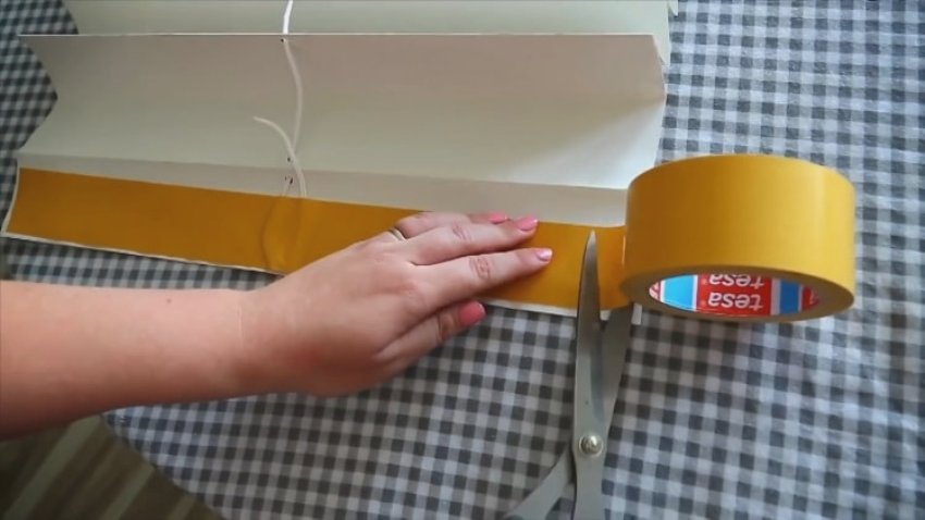 Vi fastgør rebet, der er strakt gennem alle persiennerne, med dobbeltsidet tape til folden, som er planlagt som den øverste Vi fastgør rebet, der er strakt gennem alle persiennerne, med dobbeltsidet tape til folden, som er planlagt som den øverste